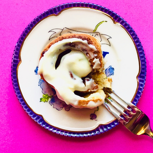 Gluten free cinnamon roll with a fork on a white and purple plate with pink background.