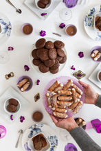 Load image into Gallery viewer, Overhead shot of a woman placing a purple dish of gluten free cannoli on a table filled with gluten free sweets, fresh flowers and decorative plates.