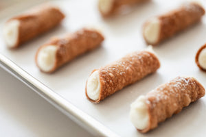 Gluten free cannoli on a baking sheet filled with ricotta filling and dusted with powdered sugar.